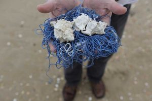 Doctor Sterman, one of the owners of a tzitzit factory, holds the strings of a blue satin worm from which the tzitzit frills are made, on the beach in Tel Aviv.